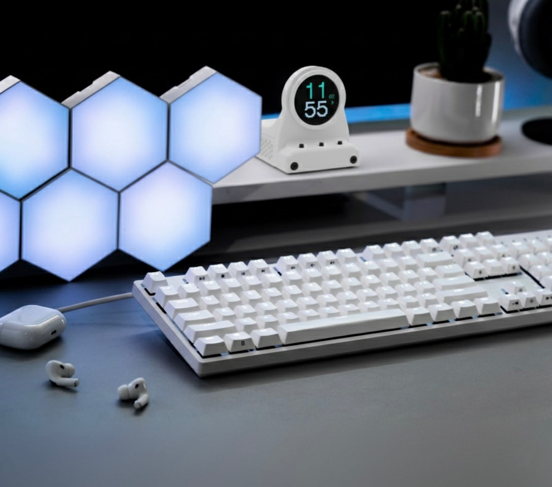 White keyboard on a desk with hexagonal light panels and a DeskOrbie in the background.